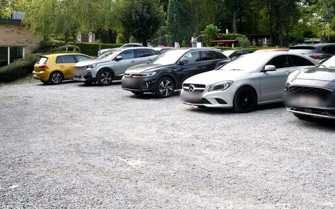 Le parking en gravier, une dizaine de voitures garées.
